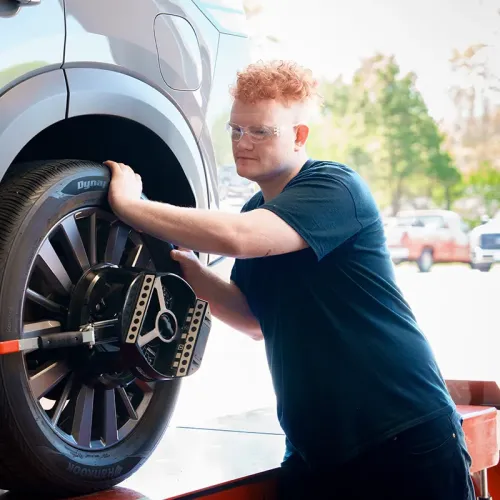 Student uses a wheel alignment tool on a tire while the vehicle is raised on a hydraulic lift